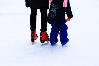 Kışın annesiyle paten pistinde kayan küçük bir çocuk. Bir kadın çocuğuna paten kaymayı öğretiyor. Spor kulüpleri, aile sporu, kış tatillerinde çocuklar için eğlence, Noel için, Yeni Yıl için