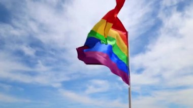 Mavi gökyüzüne ve bulutlara karşı sallanan LGBT örgütünün gerçekçi gökkuşağı bayrağı. LGBT gurur bayrakları arasında lezbiyenler, geyler, biseksüeller ve transseksüeller yer alıyor.