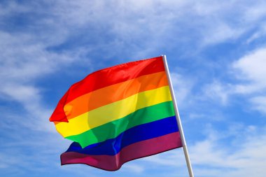 Mavi gökyüzüne el sallayan LGBT örgütünün gerçekçi gökkuşağı bayrağı. LGBT gurur bayrakları arasında lezbiyenler, geyler, biseksüeller ve transseksüeller yer alıyor.