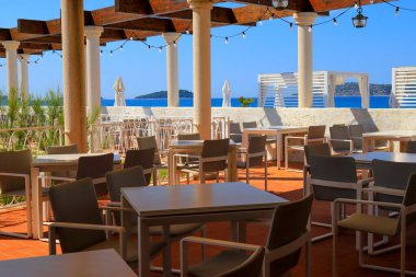 Deniz kenarında beyaz sütunları olan bir kafenin güzel resimli yaz manzarası. Kahverengi masalar Hırvat deniz manzarasının zeminine karşı. Sibenik, Hırvatistan