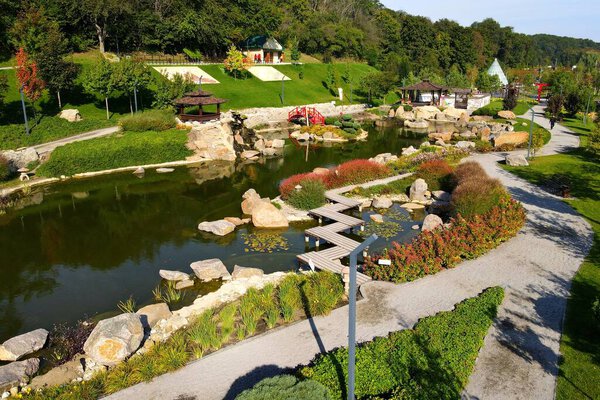 Lake in landscaped park in Japanese style. Beautiful landscape design, lake, wooden gazebos, red bridge. Aerial view of park from drone. Uman, Ukraine,