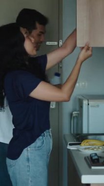 Genç çift birlikte çalışıyor, mutfak dolabından malzemeler alıyor, ev ortamında yemek pişiriyor.