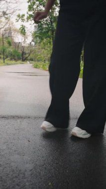 Kadın parkta siyah pantolon ve beyaz spor ayakkabı giyerek dans ediyor - 4K Yatay