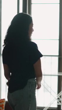 Pencerenin kenarında dans eden, müzikten hoşlanan ve kendini ifade eden kaygısız genç kadın - 4K Yatay