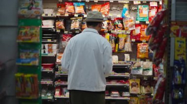 Gıda bilimci market rafları boyunca paketlenmiş ürünleri dikkatle inceliyor - 4K Yatay