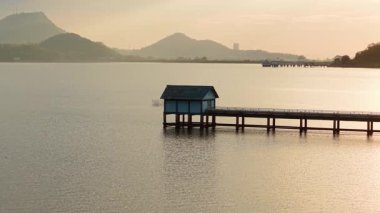 Issız bir iskele ve küçük mavi bir kulübe sisli dağların desteklediği sakin suya uzanır. Sıcak altın ışık altında - 4K yatay ışık altında.