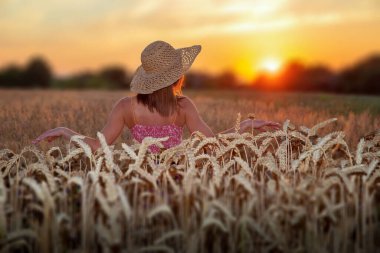 # Hasır şapkalı genç kız gün batımında buğdayın arasında #