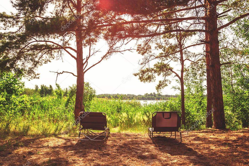 Two chairs sit on a sant beach facing the waters of a lake during a sunny summer day