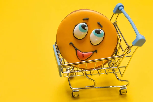 In de metalen kar van de winkel-cookies in de vorm van een glimlach, met een uitstekende tong, op een gele achtergrond, het concept van het winkelen — Stockfoto