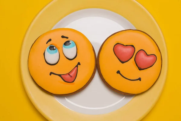 Due biscotti gialli a forma di sorriso si trovano su un piatto giallo, su uno sfondo giallo — Foto Stock