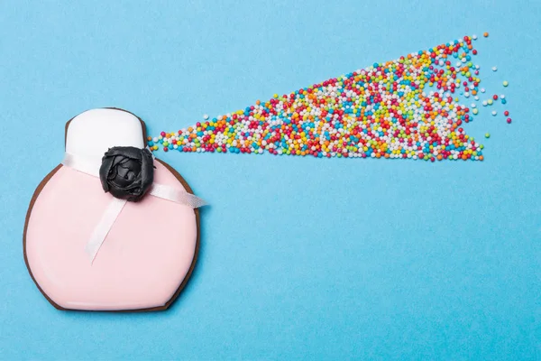 Gingerbread in the shape of a bottle for perfume on a blue background, multi-colored sweet peas are laid out in the form of an active spray, the concept — Stock Photo, Image