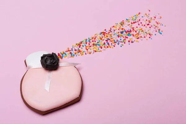 Gingerbread in the shape of a bottle for perfume on pink, next to it there are multicolored sweet candies in the form of a spray, the concept of a holiday — Stock Photo, Image