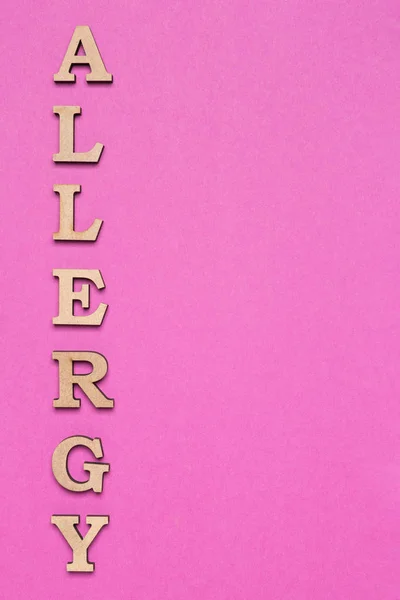На сиреневом фоне буквы выложены в слове аллергия, вертикальное расположение, минимальная концепция — стоковое фото