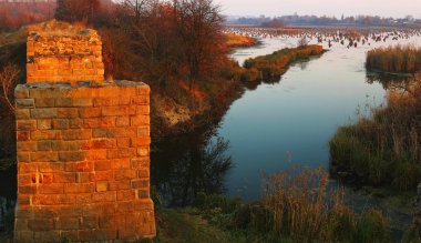 Gölde gün batımı. Gün batımı ışınları göl üzerinde bir taş köprü kalıntıları