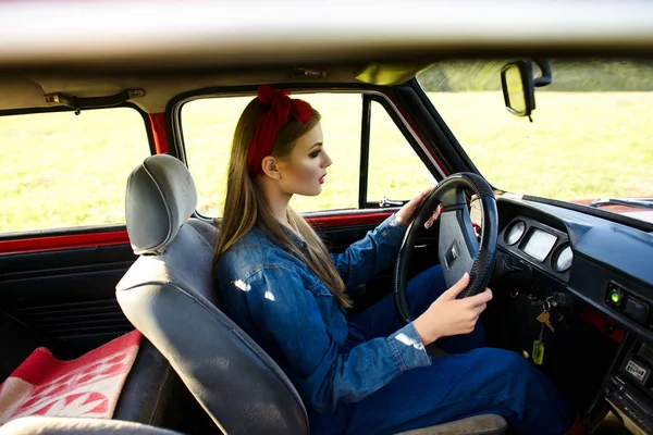 Girl dressed in denim clothes driving red old car