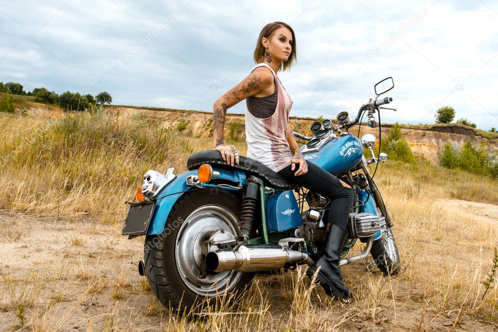 Attractive stylish dangerous girl posing with  bike in deserted nature