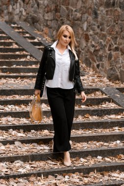 Deri ceketli, parkta poz veren güzel bir kadın.