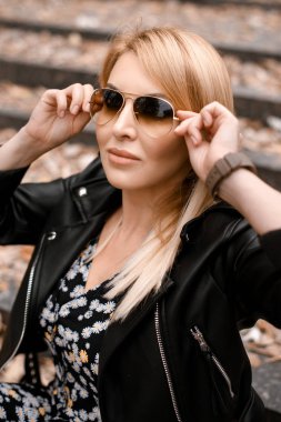 Deri ceketli genç ve güzel bir kadın merdivenlerde poz veriyor.