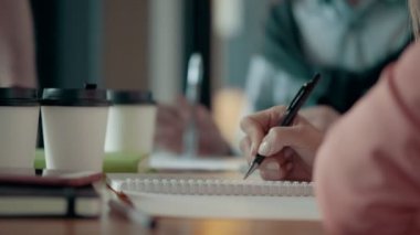 Modern ofis masası üzerinde kalem kullanarak bir not defteri notlar alarak Avrupa kadının ellerini yukarıya kapatmak