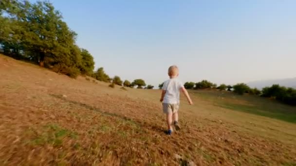 Juguetón europeo niño corriendo a lo largo de pradera al atardecer cámara lenta steadicam establecer tiro — Vídeos de Stock