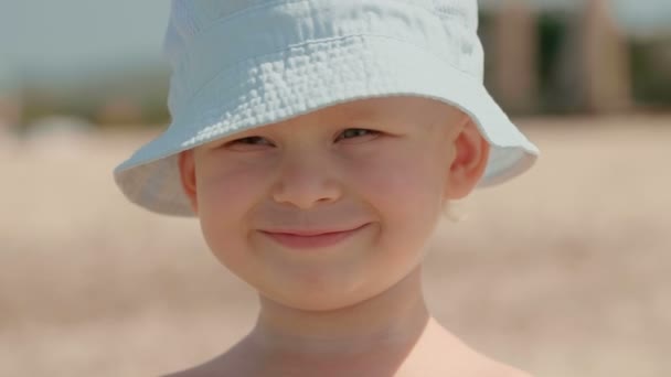 Retrato de cerca de un niño europeo sonriente con un sombrero blanco que se divierte al aire libre — Vídeo de stock
