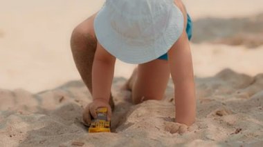 Oyuncak traktör veya Ekskavatör Kum Plajı ile oynarken erkek bebek şapka ve banyo şort