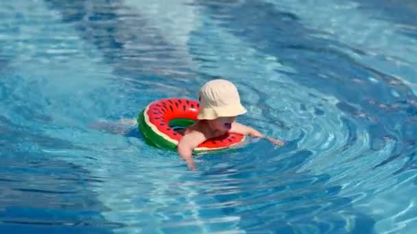 Pequeño bebé de tiro largo con sombrero flotando en la piscina con agua azul pura usando boya salvavidas — Vídeo de stock