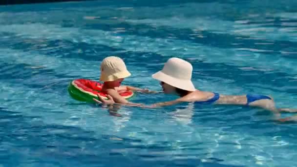 Little baby boy with caring mother wearing hat floating in outdoor swimming pool using lifebuoy — Stock Video