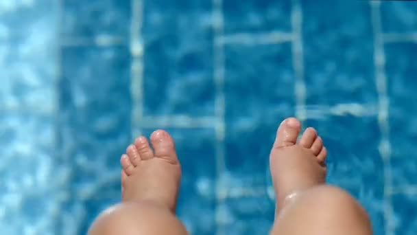 Vista superior cerca de las piernas bronceadas de lindo bebé sentado en la piscina haciendo chapoteo en agua pura — Vídeos de Stock