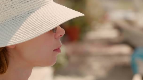 Close-up face of young tourist woman wearing hat and sunglasses relaxing on beach side view — Stock Video