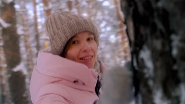 Primer plano retrato de la mujer sonriente juguetona divirtiéndose girando alrededor del tronco del árbol en el bosque de invierno — Vídeo de stock