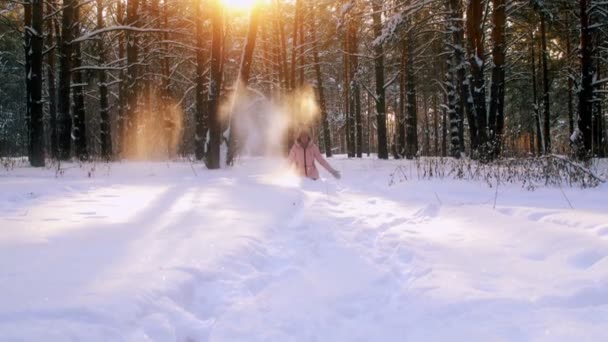 Jeune femme ludique assise dans la dérive des neiges et jouant avec des flocons de neige dans la forêt d'hiver au coucher du soleil — Video