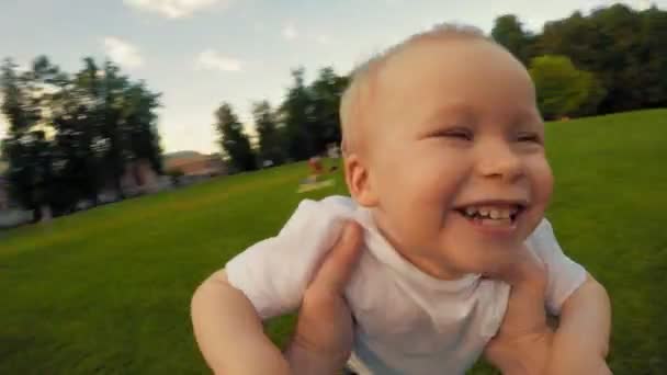 Primer plano de cara de niño lindo feliz durante el giro por las manos del padre en el parque al atardecer POV disparo — Vídeos de Stock