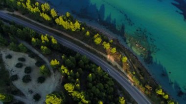 Yunanistan'da deniz sahil şeridi ve yeşil yoğun orman ile çevrili asfalt yolda hareket eden araba yukarıdan görünümü