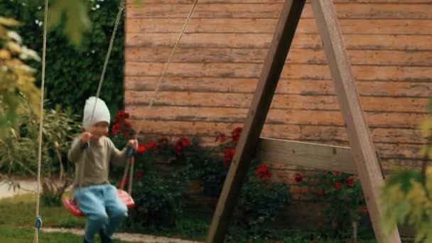 Сміється маленький милий хлопчик розважається на гойдалках, розслабляючись на дитячому майданчику повільний рух — стокове відео