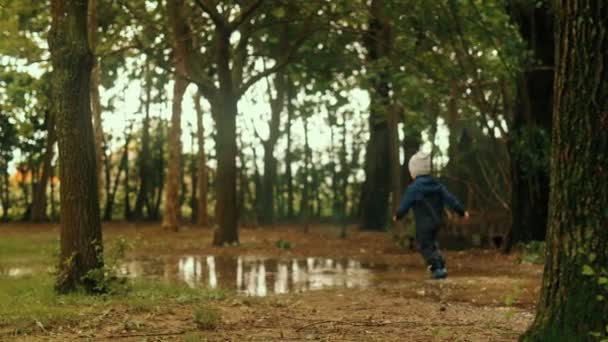 Little cute baby boy enjoying running on puddle at cold autumn raining day slow motion — Stock Video