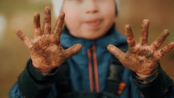 Крупним планом маленький грайливий хлопчик, що показує брудний в землі руки неслухняна дитина насолоджується щасливим дитинством — стокове відео