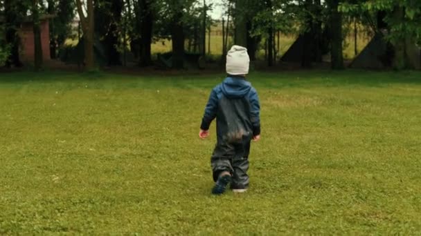 Счастливый беззаботный маленький мальчик в грязной одежде, гуляющий по зеленой траве в лесном парке — стоковое видео