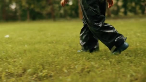 Close-up little boy legs wearing rubber boots walking on green fresh grass tracking shot slow motion — Stock Video