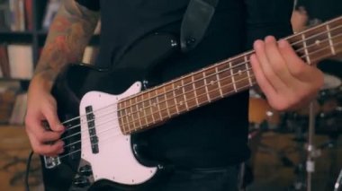 Stüdyo rock performansında bas gitar çalan erkek dövmeli basçının yakın çekim elleri.