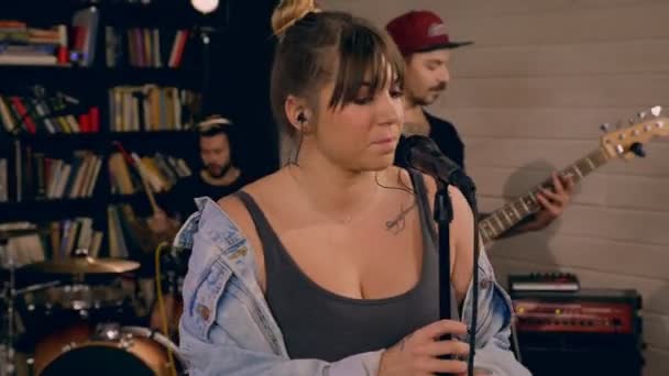 Ταλαντούχα νεαρή γυναίκα σολίστ ροκ συγκροτήματος απολαμβάνοντας το τραγούδι στο μικρόφωνο που περιβάλλεται από μουσικούς — Αρχείο Βίντεο