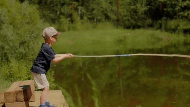 Niño activo lanzando caña de pescar tratando de atrapar peces en el lago en verano día soleado — Vídeo de stock