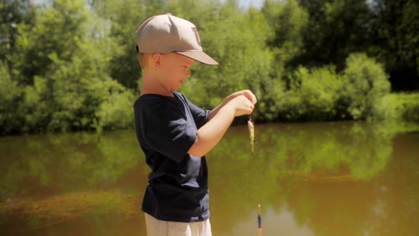 Симпатичный маленький рыбак держит маленькую рыбку на леске, улыбаясь и испытывая положительные эмоции. — стоковое видео