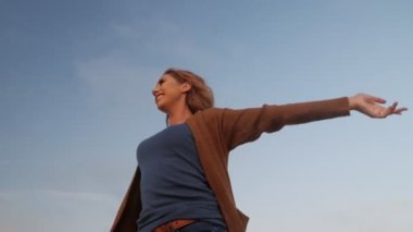 Mutlu kadın ellerini kaldırarak dönüyor. Mavi gökyüzü arka planında olumlu duygular yaşıyor.