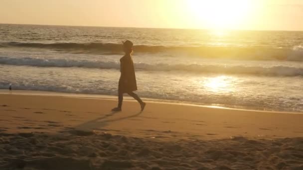 Rahat gezgin kız gün batımında sahilde yürüyen doğal deniz manzarasının tadını çıkarıyor. — Stok video