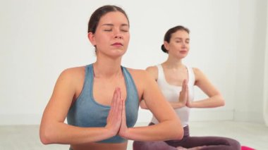 Sakinleştirici meditasyon ve rahatlama egzersizleri yapan iki kadın, dingin bir atmosferde farkındalığı, iç huzuru ve duygusal refahı destekleyen uyumlu yoga pozları sergiliyor.