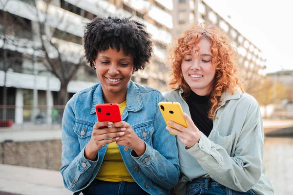 İki neşeli genç kadın, akıllı telefonlarını birlikte kullanırken, anlarını paylaşıp kahkahalar atarak derin bir sohbete daldılar. Keyifleri, cep telefonuyla beslenen bağlantıyı yansıtıyor
