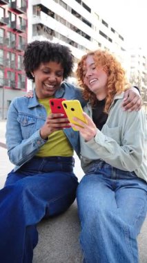İki hayat dolu genç kadın, bu canlı ve anlamlı fotoğrafta neşeli bir şekilde akıllı telefonlarıyla gülüşlerini ve keyifli anlarını paylaşıyor, arkadaşlıklarını ve bağlantılarını sergiliyor..