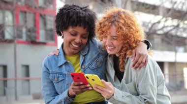 İki neşeli genç kadın, akıllı telefonlarını birlikte kullanırken, anlarını paylaşıp kahkahalar atarak derin bir sohbete daldılar. Keyifleri, cep telefonuyla beslenen bağlantıyı yansıtıyor