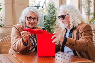 Mutlu son sınıf çifti neşe ve beklentiyle dolu kırmızı bir hediye kutusunu açmaya can atıyor. İfadeleri, özel bir anı paylaşmanın sevincini gözler önüne seriyor. Bağlarını ve sevgilerini güçlendiriyor.